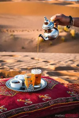 a person is pouring coffee into a cup on a table at ERG merzouga desert Luxury camp in Merzouga
