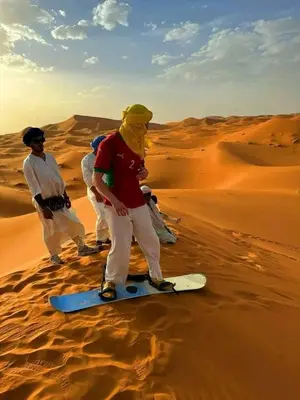 a group of people standing on a snowboard in the desert at ERG merzouga desert Luxury camp in Merzouga