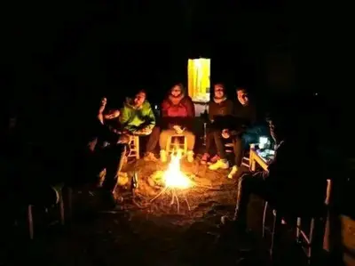 a group of people sitting around a fire in the dark at ERG merzouga desert Luxury camp in Merzouga