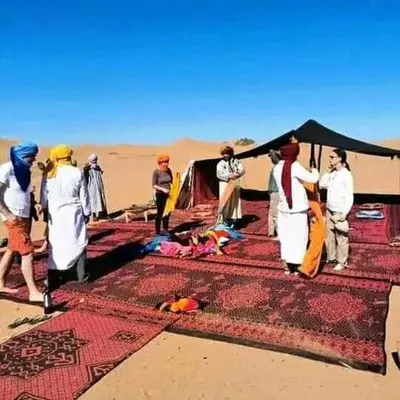 a group of people standing around a tent in the desert at ERG merzouga desert Luxury camp in Merzouga