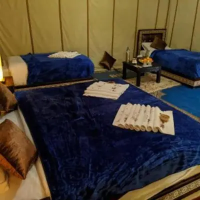 a room with two beds and a table in a tent at fabulousluxurycamp in Merzouga
