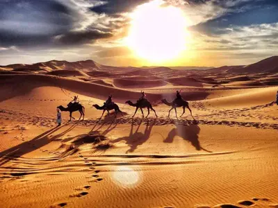 a group of people riding camels in the desert at Morocco Tour Itineraries in Merzouga