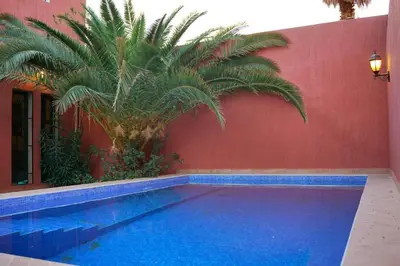 a swimming pool with a palm tree next to a red wall at Villa Zazate private pool & starry garden in Ouarzazate