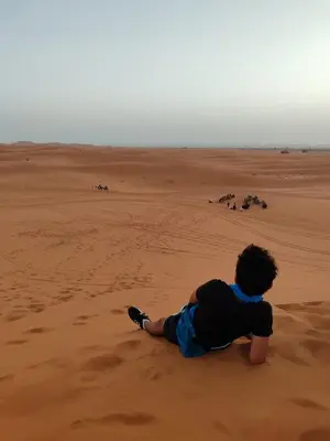 a boy sitting on the sand in the desert at Auberge merzouka in Rissani