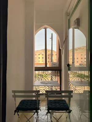 a table and two chairs in a room with two windows at Appartement Marrakech in Oulad Akkou