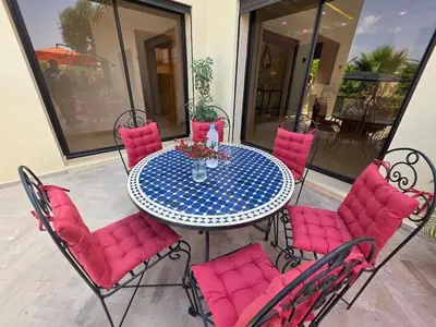 a table with pink cushioned chairs around it on a patio at Villa Nomade Residence 3 chambres avec piscine in Oulad Snaguia