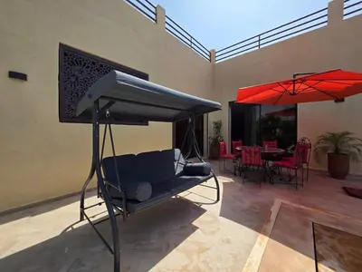a porch with a swing and red umbrellas at Villa Nomade Residence 3 chambres avec piscine in Oulad Snaguia
