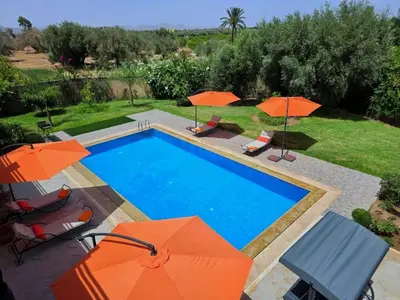 a swimming pool with orange umbrellas and chairs at Villa Nomade Residence 3 chambres avec piscine in Oulad Snaguia