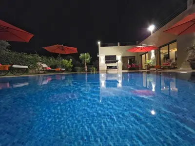 a large blue swimming pool at night with red umbrellas at Villa Nomade Residence 3 chambres avec piscine in Oulad Snaguia