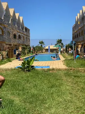 a resort swimming pool with people laying in the grass at Maison villa in Oulad Akkou