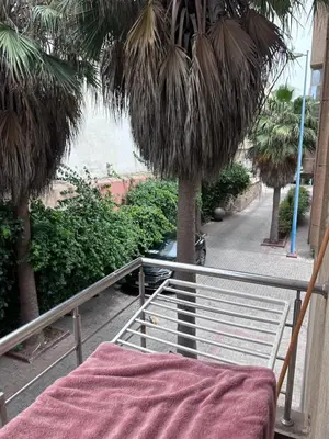 a balcony with a bed and palm trees on a street at Appartment propre in Oulad Akkou