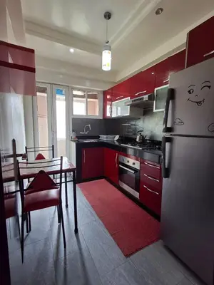 a kitchen with red cabinets and a table and a refrigerator at yas appart in Oulad Akkou