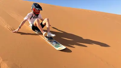 a man riding a snowboard down a sand dune at lina safari luxury camp in Merzouga