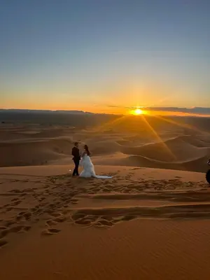 a bride and groom walking in the desert at sunset at lina safari luxury camp in Merzouga