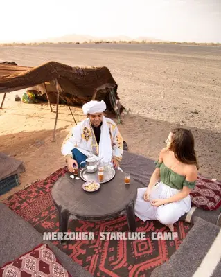 a man and a woman sitting at a table on the beach at Merzouga Starluxe Camp in Merzouga