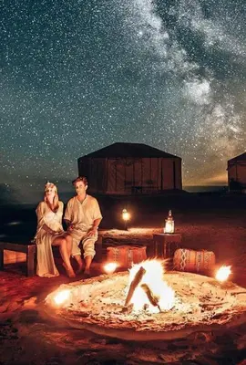 three people sitting around a fire pit under a starry sky at Host Luxury Camp in Merzouga