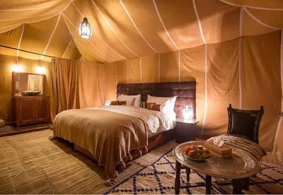 a bedroom with a bed and a table in a tent at Host Luxury Camp in Merzouga