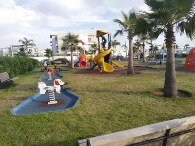 a park with a playground with slides and palm trees at Appartement dans une résidence balnéaire à Sidi Rehal in Oulad Akkou