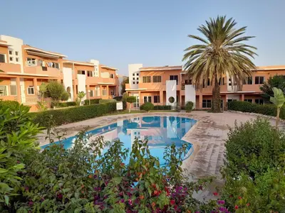 a swimming pool in front of a building with a palm tree at Village al baraka in Oulad Akkou