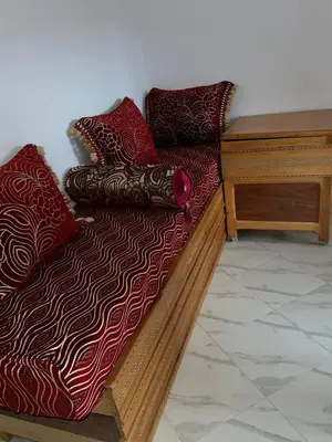 a wooden bed with red pillows and a wooden table at Appartement in Oulad Akkou