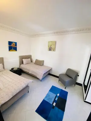 a room with two beds and a chair and a blue rug at Villas Appart Hotel in Oulad Akkou