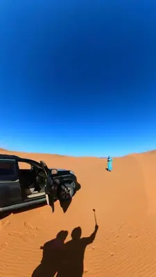 a shadow of two people and a car in the desert at desertcamp in Merzouga