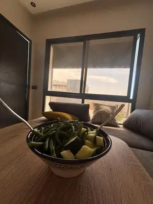 a bowl of green vegetables on a table with a window at Chambre, appartement Anas in Oulad Akkou