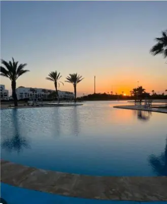 a pool of water with palm trees and a sunset at Le séjour idéal in Oulad Akkou