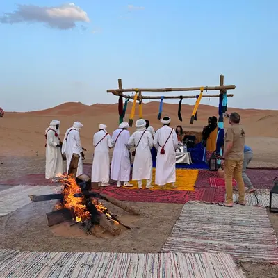 a group of men standing around a fire in the desert at Luxury camps merzouga in Merzouga