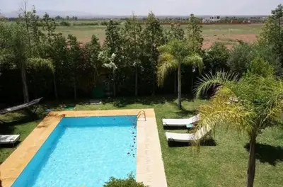 a swimming pool in a yard with two chairs and trees at Villa Flower in Oulad Akkou