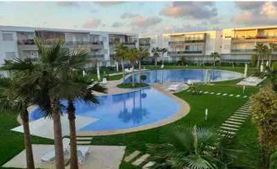 an apartment complex with a swimming pool and palm trees at Sidi rahal Blanca beach in Zaouia Sidi Rahkal