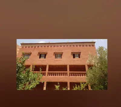 a tall brick building with trees in front of it at Gite le Calme café Restaurant Pizzeria in Bou Tharar