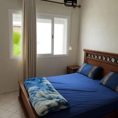 a bedroom with a bed with blue sheets and a window at résidence ichraka in Oulad Akkou