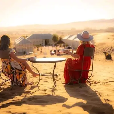two women sitting at a table in the sand at Merzouga Hosting & Camelride in Merzouga
