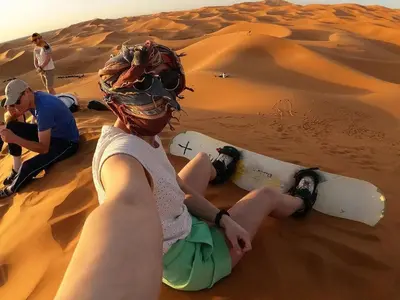 a woman sitting in the desert with a snowboard at Merzouga Eastern Camp Luxury in Merzouga