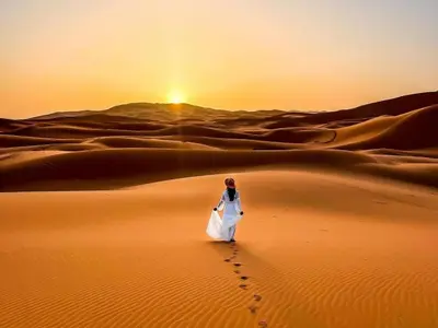a man walking through the desert at sunset at Merzouga Eastern Camp Luxury in Merzouga
