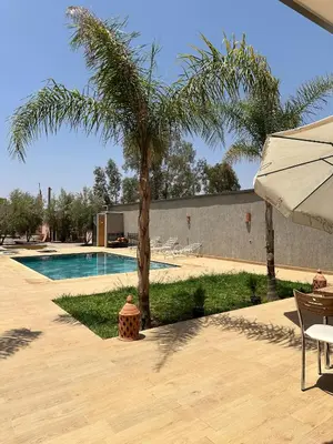 a swimming pool with a palm tree and an umbrella at villas par jour in Amezrou