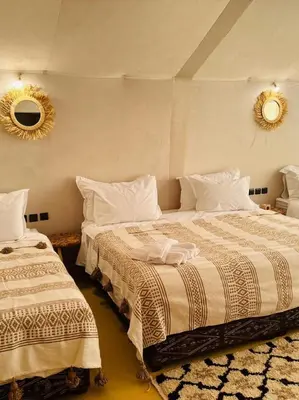 a bedroom with two beds and a mirror on the wall at Sunlight Luxury Desert Camp in Merzouga
