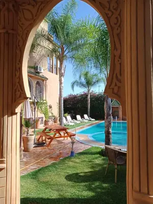 an archway in a house with a pool and a table at Les Jardins de Ryad Bahia in Meknès