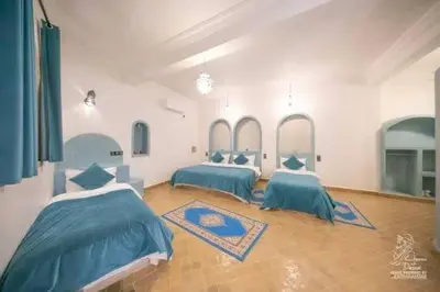 two beds in a large room with blue sheets at Hotel Dar Sahara in Merzouga