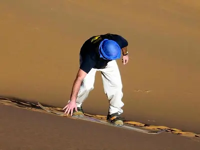 a man standing on a snowboard on the ground at Shahrazad Nights Desert Camp in Merzouga