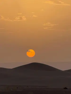 an orange moon in the sky over a field at Arawan Luxury Desert Camp at Erg Lihoudi in Mhamid