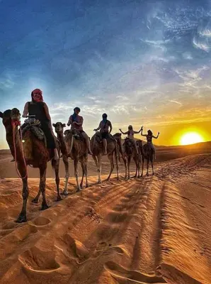 a group of people riding camels in the desert at Tenere luxury camp in Merzouga