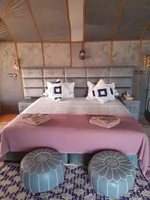 a bedroom with a large bed with two ottomans at Merzouga Solace Luxury Camp in Merzouga