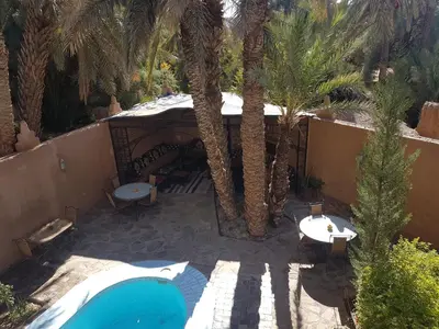 an outdoor patio with a swimming pool and palm trees at Rose du Sable in Agdz