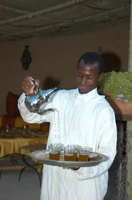 a man holding a tray of glasses of beer at Rose du Sable in Agdz