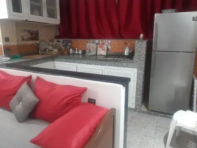 a kitchen with a couch with red pillows and a refrigerator at Jolie Appartement Confortable - près de la plage in Oulad Akkou