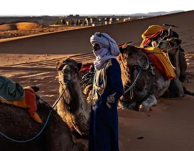 a man standing next to a group of camels in the desert at Sahara Authentic Camp in Merzouga