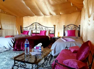 a room with two beds and a table in a tent at Merzouga Lovely Luxury Camp in Merzouga