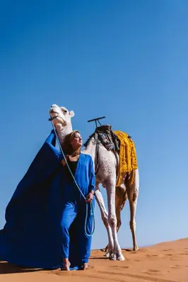 a woman standing next to a camel in the desert at Riad Serai Merzouga in Merzouga